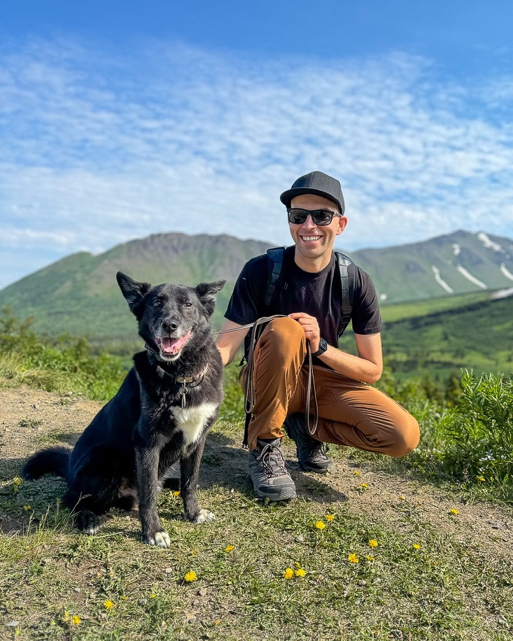 Aaron Jokela crouched beside his black dog on a Pacific Northwest mountain ridge
